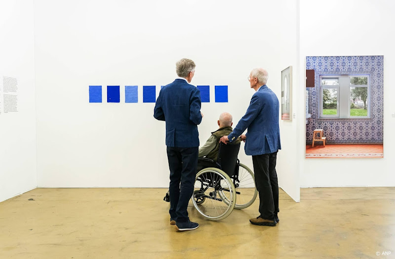 man in rolstoel met twee andere mannen bij kunstwerk